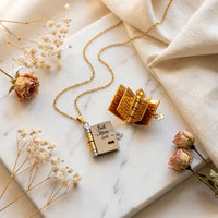 Best Mom Ever book locket necklace open showing 
golden engraved pages on marble with dried roses 
and baby's breath — luxury heartfelt mom gift
