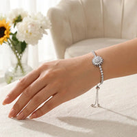 Woman wearing silver crystal sunflower bracelet with 
tennis chain on wrist resting cream linen wellness jewelry