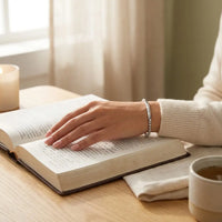 Woman wearing God Is Within Her silver bracelet 
while reading Bible — peaceful prayer 
mindfulness daily faith reminder