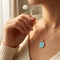 Woman wearing golden cross pendant necklace with turquoise 
blue stone center 14K gold faith jewelry