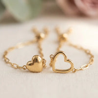 Macro detail of matching gold heart charms 
— solid heart and open heart silhouette 
side-by-side — premium dainty bracelet set
