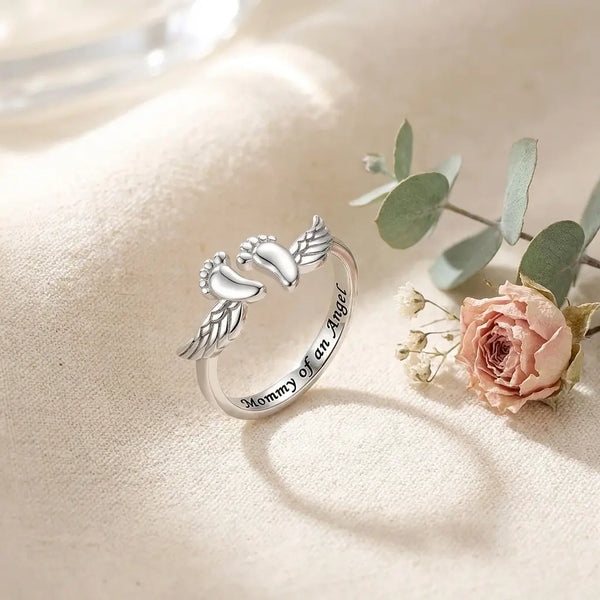 Mommy of an Angel sterling silver memorial 
ring with angel wings and baby feet on cream 
linen — meaningful keepsake for angel moms 
and pregnancy loss