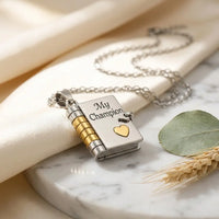 Macro detail of My Champion engraving on silver 
and gold book locket pendant with heart accent — 
heartfelt mother son keepsake jewelry