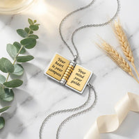 My Champion book locket necklace open showing 
engraved pages Your heart is your compass on 
white marble with eucalyptus — luxury heartfelt 
son gift