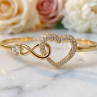Macro detail of gold infinity loop and hollow pavé 
crystal heart centerpiece on To My Daughter bangle 
bracelet — premium luxury jewelry detail
