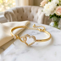 To My Daughter infinity heart bangle bracelet in 
gold with pavé crystal heart and interlinked 
infinity loop on white marble — sentimental mother 
daughter gift