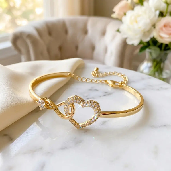 To My Daughter infinity heart bangle bracelet in 
gold with pavé crystal heart and interlinked 
infinity loop on white marble — sentimental mother 
daughter gift