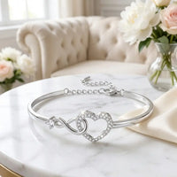 To My Daughter infinity heart bangle bracelet in 
silver with pavé crystal heart and interlinked 
infinity loop on white marble — sentimental mother 
daughter gift