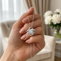 Silver love knot pendant held gently in fingers showing 
crystal sparkle and chain detail